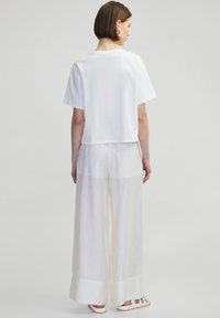 White cropped t-shirt with short sleeves paired with lightweight, sheer, pleated white trousers and white strappy sandals.