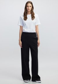 Witte t-shirt met korte mouwen in combinatie met zwarte hoge taille broeken met wijde pijpen. De broeken hebben een zachte textuur en een subtiele voorplooi.