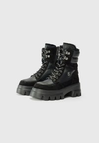 Bottes à lacets noires élégantes avec une semelle à plateforme, présentant un mélange de textures en cuir et en suede et des accents métalliques décoratifs.