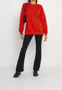 Röd överdimensionerad sweatshirt med ribbade muddar och nederkant, i kombination med svarta utsvängda byxor och svarta skor. Inkluderar en liten svart handväska.