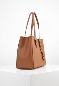 Sac cabas en cuir marron avec une forme structurée, une base plate, deux longues anses et des accents en métal doré. Surface texturée et design élégant.