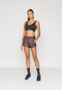 Zwarte sportbeha met wit logo, gecombineerd met bruine shorts met luipaardprint, voorzien van een elastische tailleband en zijzakken. Zwarte sneakers en sokken.
