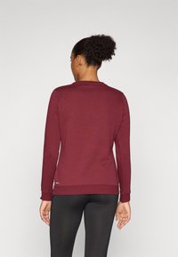 Bordeaux langermet genser med rund hals, ribbede mansjetter og nederkant, laget av et mykt stoff, brukt med svarte tights.