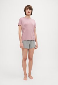 Haut rose clair à manches courtes avec des poignets retroussés associé à un short gris texturé. Les deux vêtements ont une coupe décontractée et un design simple.