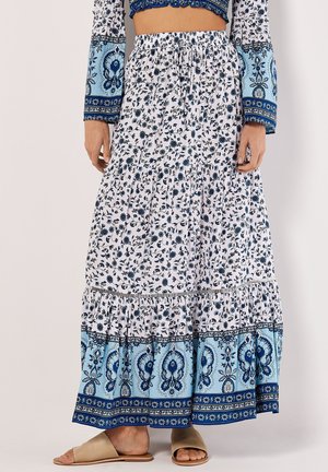 Weißer Maxirock mit blauen Blumenmustern und Paisley-Akzenten, mit einem gestuften Design und elastischem Bund, kombiniert mit beigen Sandalen.