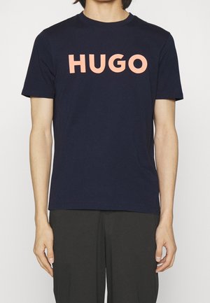 Navy blue cotton t-shirt featuring bold, light pink "HUGO" lettering on the front. Short sleeves and classic crew neckline.