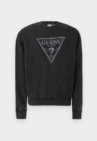 Melns kapucis krekls ar trīsstūra pelēku logo, kurā rakstīts "GUESS" un "ORIGINALS". Ribotas piedurknes un apakšmalas ar mīkstu tekstūru.