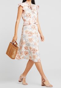 Blommig midiklänning med volangärmar och en kjol med rosett i ljuskräm, rosa och blå nyanser; matchad med en handväska i bambu och beige klacksandaler.