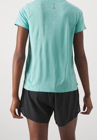 Tyrkysové sportovní tričko s krátkými rukávy a texturovaným vzorem, doplněné černými šortkami s průhlednými bočními panely.