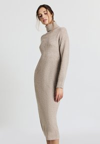 Robe en tricot à col roulé beige clair. Silhouette ajustée, manches longues, poignets et ourlet côtelés, longueur mi-mollet, texture douce.