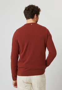 Maglione rosso lavorato a maglia con maniche lunghe, scollatura rotonda e un piccolo accento metallico sul retro. Tessuto morbido e orlo a coste.