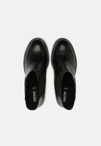 Svarta läderskor utan snörning med en slät yta, elastiska sidopaneler och en vadderad innersula. Har GEOX-logotypen på det inre foderet.