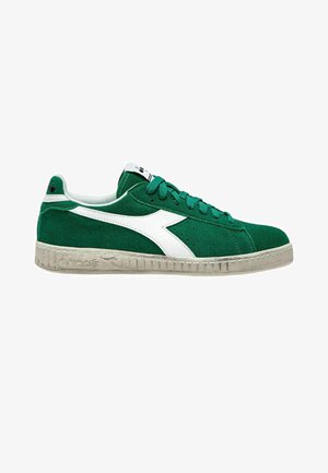 Sneaker in suede verde con accenti in pelle bianca e suola in gomma grigia testurizzata. Presenta lacci rotondi e un'etichetta con il marchio sulla linguetta.