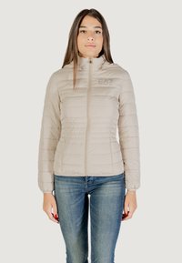 Giacca puffer beige con design trapuntato, zip completa, colletto alto e logo ricamato. Materiale leggero e silhouette aderente.