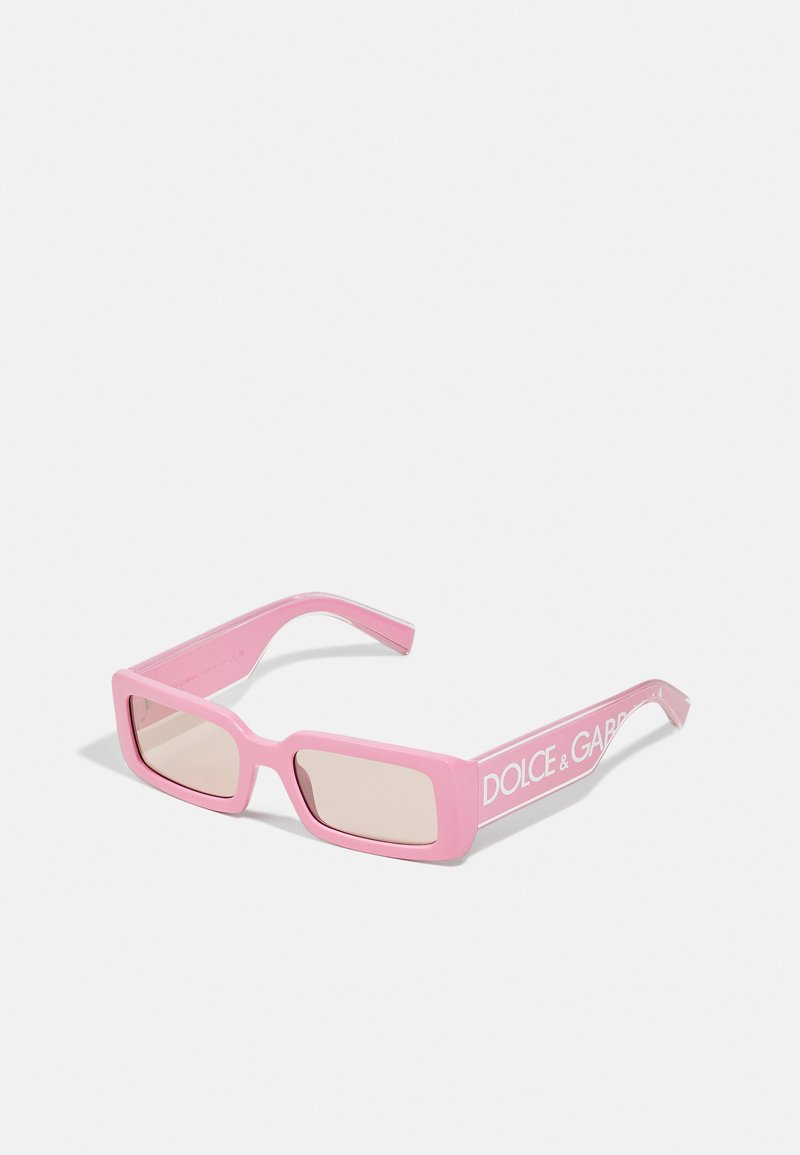 Gafas de sol rectangulares rosas con acabado mate, que presentan lentes tintados y un logo blanco en el lateral. Patillas delgadas y planas.