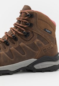 Bruine leren wandelschoen met roze accenten, gestructureerd oppervlak, zwarte veteroogjes en een grijze rubberen zool. Grote merknaam op de zijkant.