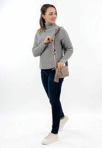 Šedý žebrovaný svetr, tmavě modré skinny džíny a bílé tenisky. Malá béžová kabelka přes tělo s třásněmi. Jednoduchý, městský ležérní outfit.