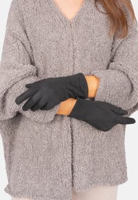 Schwarze Handschuhe aus weichem Material mit glatter Textur. Getragen von einer Person mit einem hellgrauen, flauschigen Pullover.