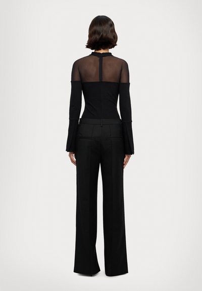 Haut à manches longues noir avec un dos transparent, design ajusté et manches évasées, associé à un pantalon noir taille haute avec des jambes droites.