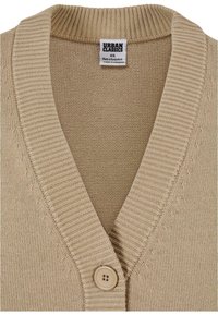 Beige knitted cardigan featuring a v-neck, ribbed edges, and a single button closure. Tag shows "Urban Classics," size XS.