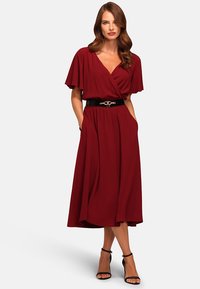 Burgundy midimekko, jossa on lyhyet leijuvaselkäiset hihat, kietaisumalli, elastinen vyötärö, sivutaskut ja musta vyö metallikoristeilla; sileä kangas.