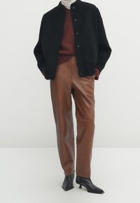 Veste en laine noire avec col arrondi, pull en tricot marron, pantalon en cuir marron et bottines noires à talon aiguille. Design simple et structuré.