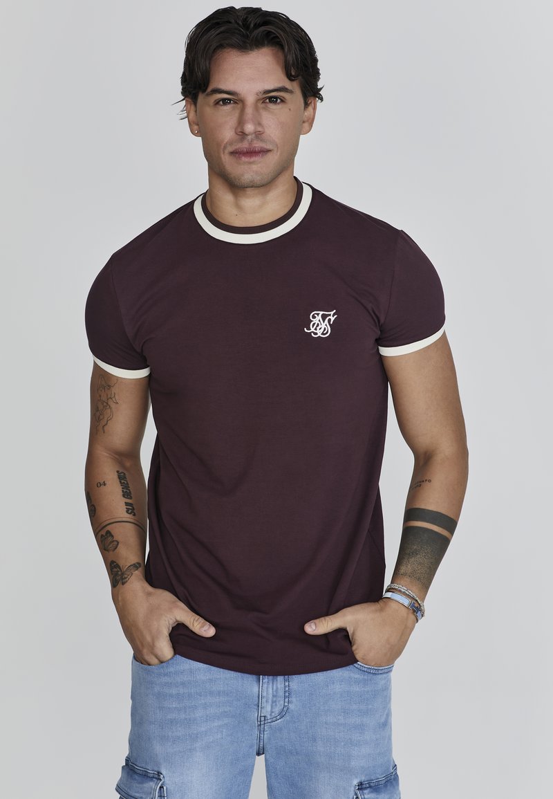 Bordeaux t-shirt met crèmehals en mouwafwerkingen, voorzien van een klein wit logo op de borst. De stof lijkt glad, met een ontwerp met korte mouwen.