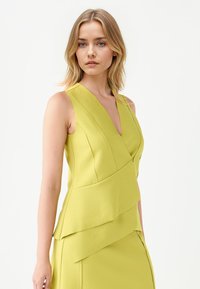 Limoengroene, mouwloze jurk met een V-halslijn, voorzien van gelaagde ruches langs de taille en een gladde textuur.