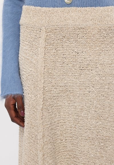 Beige textured skirt with a woven pattern, featuring a soft, slightly fuzzy finish, paired with a light blue, mohair-blend sweater.