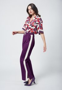 Kwiatowa bluzka z krótkim rękawem, z czerwonymi i purpurowymi wzorami; połączona z purpurowymi spodniami z białymi bocznymi paskami i purpurowymi szpilkami.