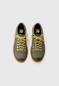 Pair of olive green hiking shoes with yellow laces, black toe caps, and brown soles, viewed from above on a white background.