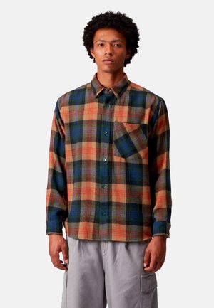 Camisa de franela a cuadros con cuadrados verdes, naranjas y azul marino, con botón delantero, un bolsillo en el pecho y un corte relajado. Textura suave.