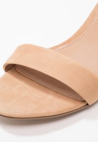 Sandale beige en daim à bout ouvert avec une large bride unique à l'avant et des coutures visibles le long du côté intérieur.