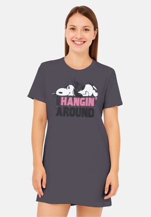 Young woman smiling, wearing a dark dress with Snoopy lying down and text "Just Hangin' Around" on the front.