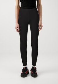 Leggings neri con una vestibilità aderente, realizzati in materiale elasticizzato; abbinati a sneaker nere e rosse e calze bianche. Design semplice, senza motivi.