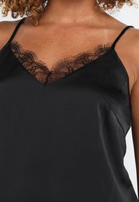 Camisole en satin noir avec des fines bretelles, présentant un décolleté en V ornée de dentelle noire pour plus de détails et de texture.