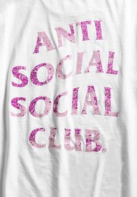 Biała bawełniana koszulka z dużym, zniszczonym różowym napisem "ANTI SOCIAL SOCIAL CLUB". Prosty, nieozdobiony design.