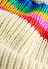 Knit sweater with ribbed texture in cream, featuring colorful horizontal stripes in red, pink, green, yellow, and blue.