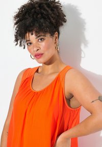 Top senza maniche di un brillante arancione con dettagli arricciati, scollatura rotonda e vestibilità ampia. Tessuto liscio con una leggerissima lucentezza.