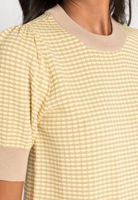 Sweter z dzianiny w kratę w jasnym żółtym i taupe, z krótkimi puffowanymi rękawami i ribbowym beżowym kołnierzykiem. Teksturowany materiał.