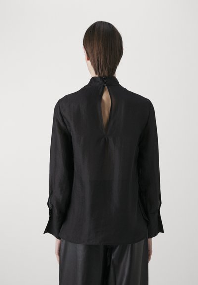 Maglia a maniche lunghe nera in un tessuto morbido e leggero. Presenta una schiena a chiave con chiusura a bottone e polsini sagomati.
