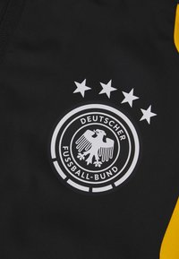 Sort stof med et hvidt logo for den tyske fodboldforening, der viser en ørn og fire stjerner ovenover.