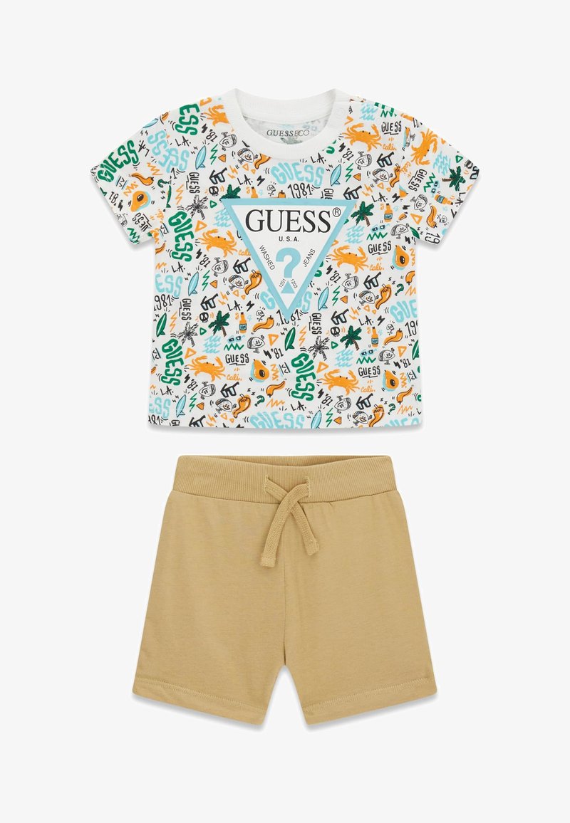 Kleinkind-Set mit einem weißen Kurzarmshirt, das bunte, strandbezogene Grafiken und das "GUESS"-Logo zeigt, kombiniert mit schlichten beigen Shorts mit Kordelzug.