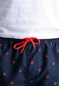 Pantaloni da mare blu navy con finitura testurizzata, caratterizzati da motivi di sole rosso e onde. Corda regolabile rossa in vita per una vestibilità ottimale.