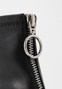 Botte en cuir noir avec une fermeture éclair en métal argenté et un tirette circulaire. Présente une finition texturée et des coutures visibles le long de la ligne de fermeture.