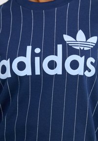 Navyblå bomullströja med vertikala vita ränder, med en ljusblå "adidas"-logotyp och tre-stripes-logotyp på bröstet.