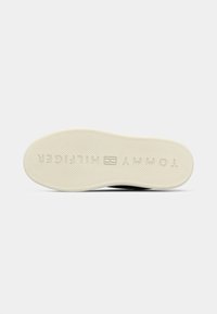 Talpă de pantof neagră din cauciuc, cu model texturat antiderapant și logo embosat "TOMMY HILFIGER" în culoare crem. Formă rotunjită cu margini netede.