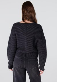 Donkergrijze gebreide trui met een geribbeld patroon, brede mouwen en een cropped pasvorm. Gecombineerd met zwarte high-waisted jeans.