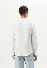 Witte blouse met lange mouwen, een rugpand, een gebogen zoom en knopenmanschetten. Gepaard met lichtblauwe rechte jeans. Eenvoudig en minimalistisch design.