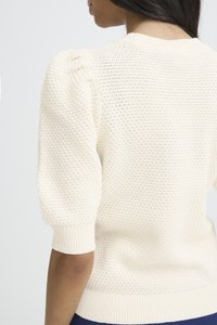 Frau trägt einen cremefarbenen, strukturierten Strickpullover mit halblangen Puffärmeln und gerippten Bündchen, von hinten und von der Seite gesehen.